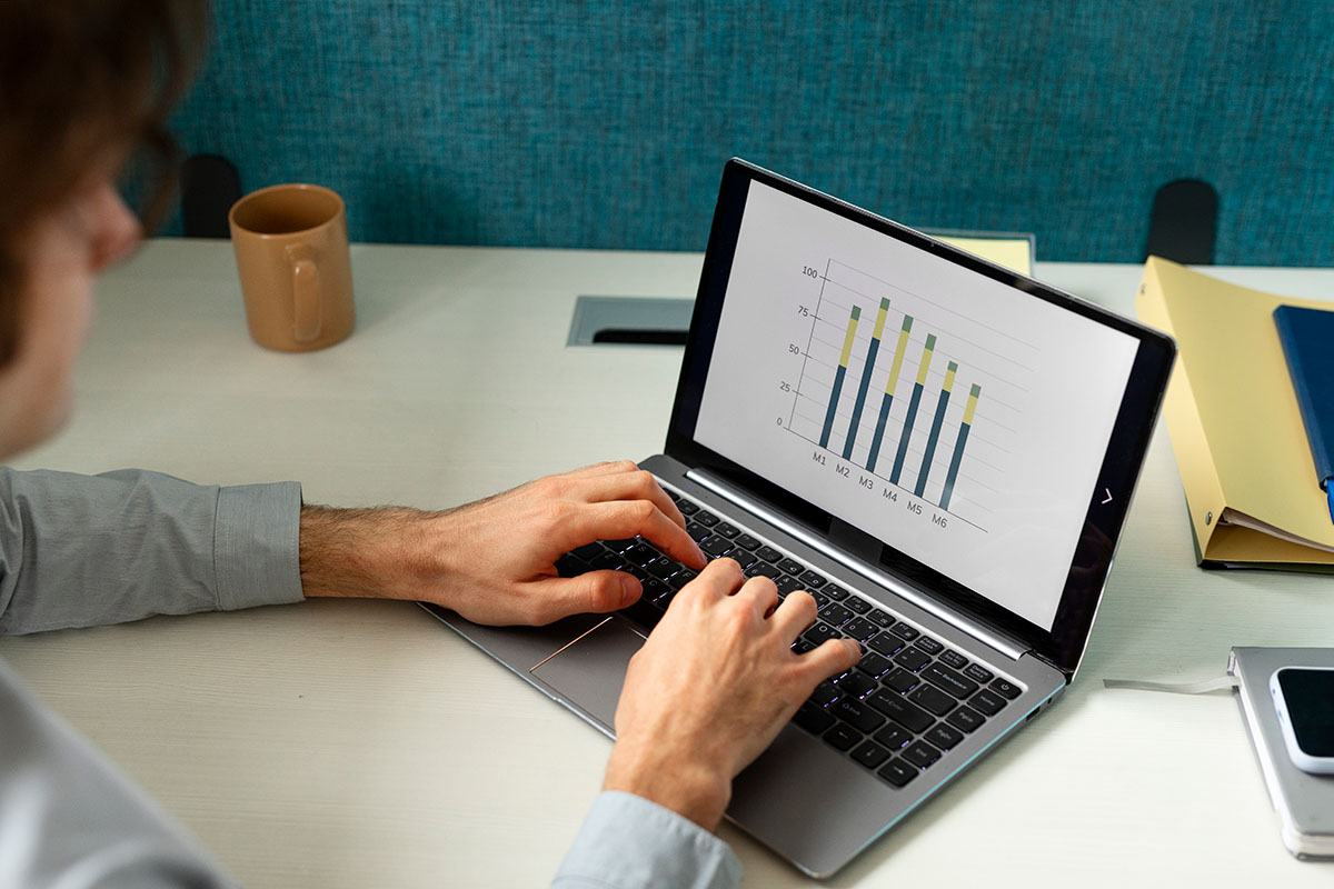 Homem de perfil digitando em um laptop com um gráfico de barras colorido exibido na tela.